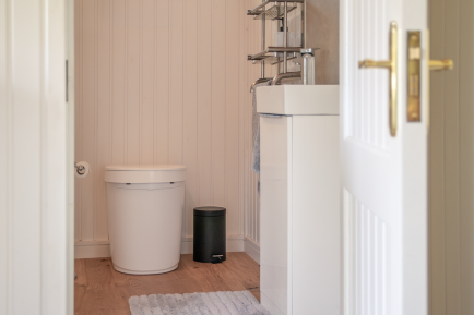 Compact toilet in a garden room View through a panelled doorway into a compact bathroom with toilet, white vanity unit and wooden flooring.